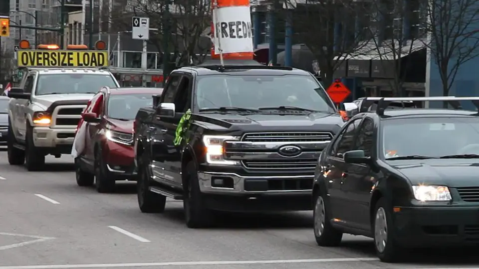 Deux camionnettes et deux voitures participent à une manifestation sur l'avenue Broadway à Vancouver.