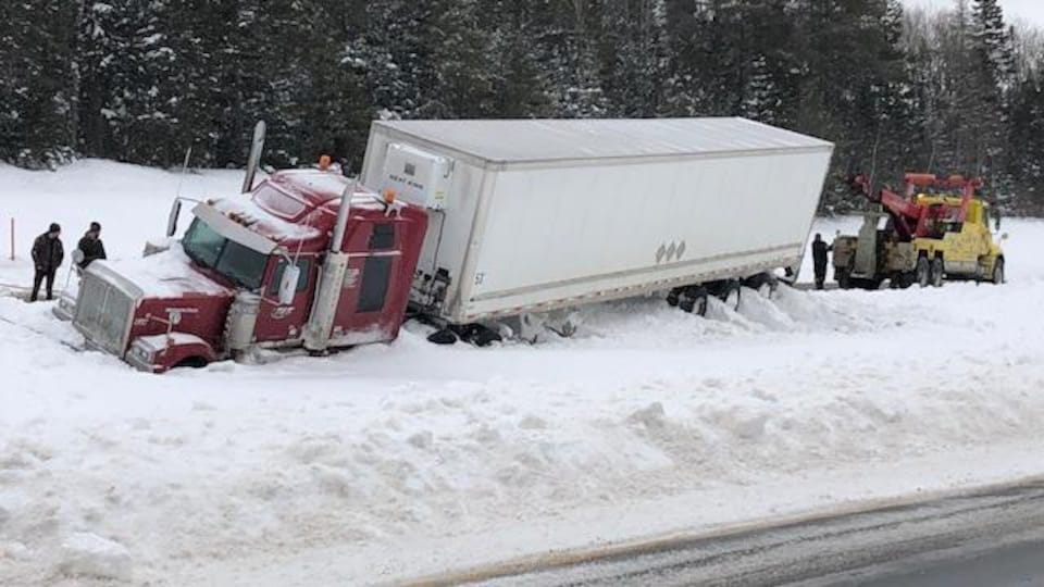 Un camion semi-remorque pris dans un haut banc de neige en bordure de l'autoroute.