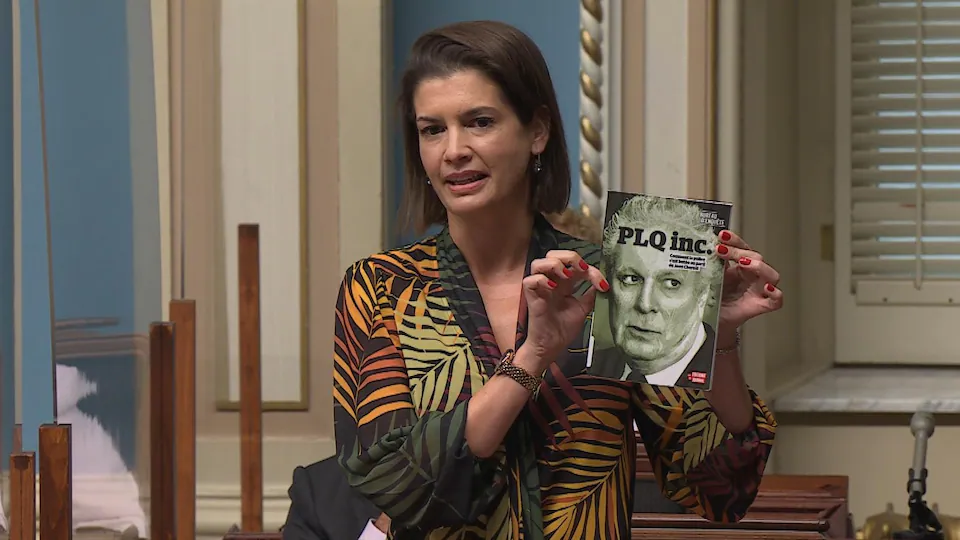 Geneviève Guilbault, debout à l'Assemblée, tient un livre avec Jean Charest sur la couverture.