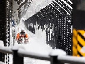 A city worker clears snow off the walkways of the High Level Bridge after a morning snowstorm in Edmonton, on Friday, March 4, 2022.