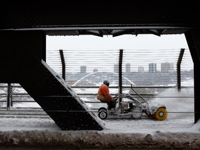 A city worker clears snow off the walkways of the High Level Bridge after a morning snowstorm in Edmonton, on Friday, March 4, 2022.