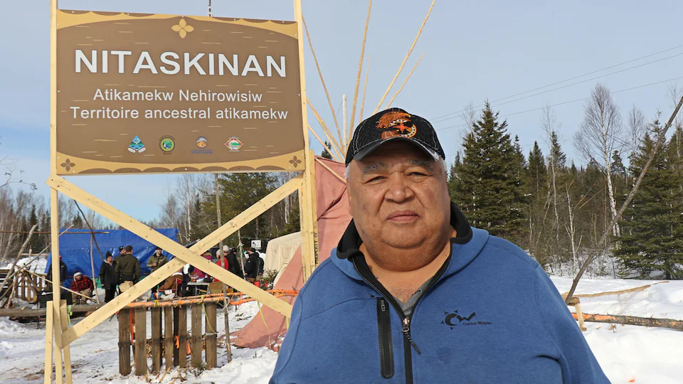 Un homme pose devant un panneau avec l'inscription Nitaskinan, Territoire ancestral atikamekw.