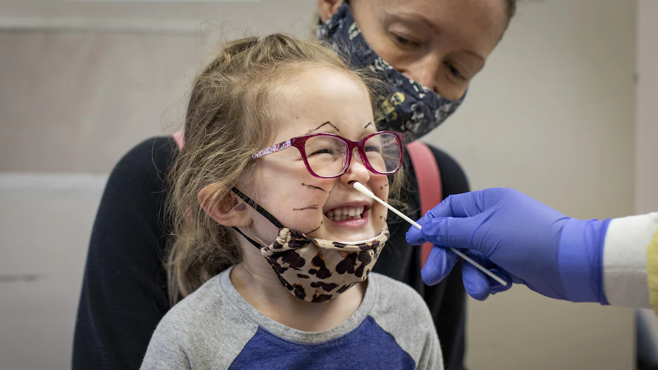 Une fillette ferme les yeux, alors qu'on lui insère dans le nez une tige de prélèvement pour un test de dépistage.