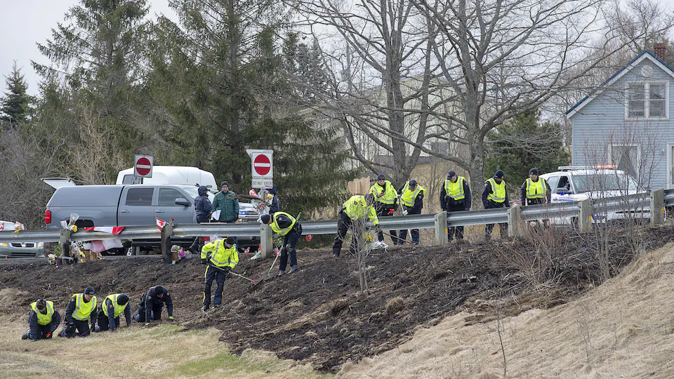 Une douzaine de policiers, certains debout et d'autres à genoux, examinent les lieux d'un accident et d'un meurtre près de l'autoroute.