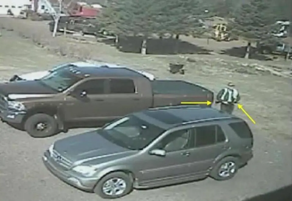 Image d'une caméra de surveillance. On voit un homme qui semble armé s'avancer dans le stationnement, passant près de deux véhicules stationnés.