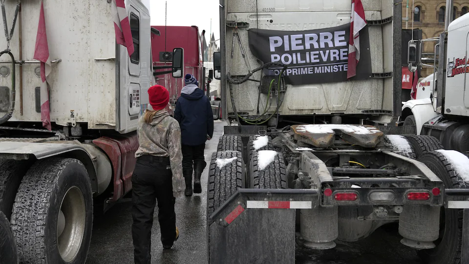 Des personnes passent près d'un camion portant un drapeau appelant le député conservateur Pierre Poilievre à devenir premier ministre lors de l'occupation d'Ottawa en février.