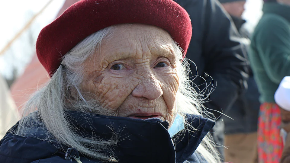 Une vieille dame avec un béret rouge sur la tête.