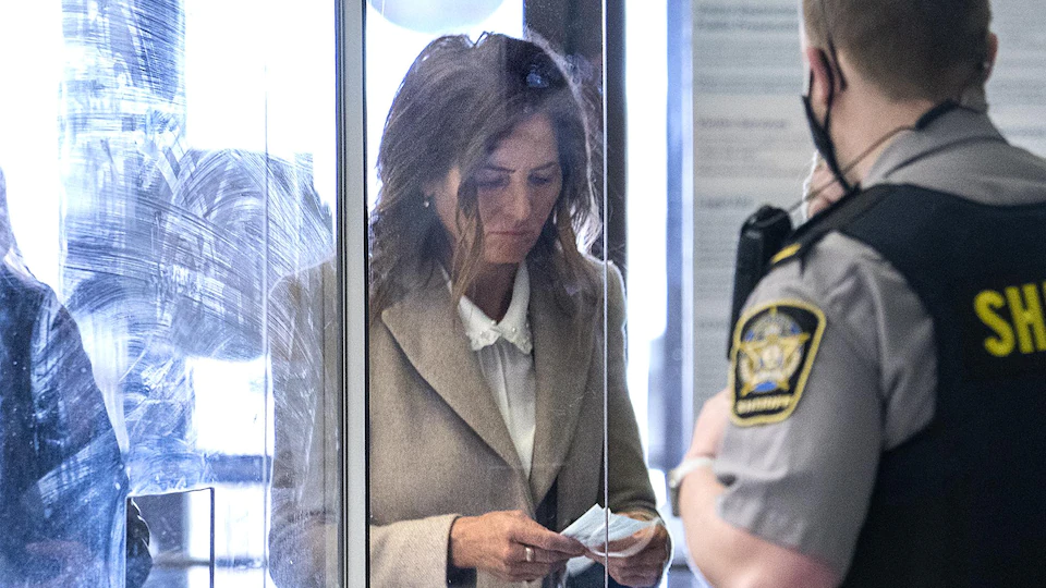 Lisa Banfield avec un masque dans les mains entre au palais de justice en passant devant des agents de sécurité.