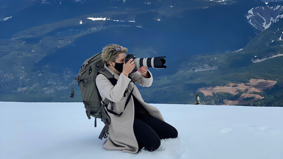 Pascale Anouk Rivest-Gadbois est agenouillée sur un sommet enneigé en train de prendre une photo. 