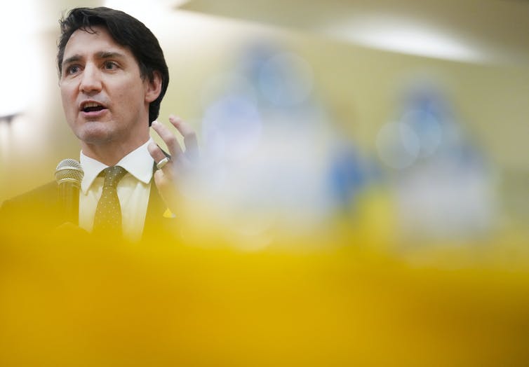 A man with dark hair talks with the yellow of the Ukrainian flag in the foreground.
