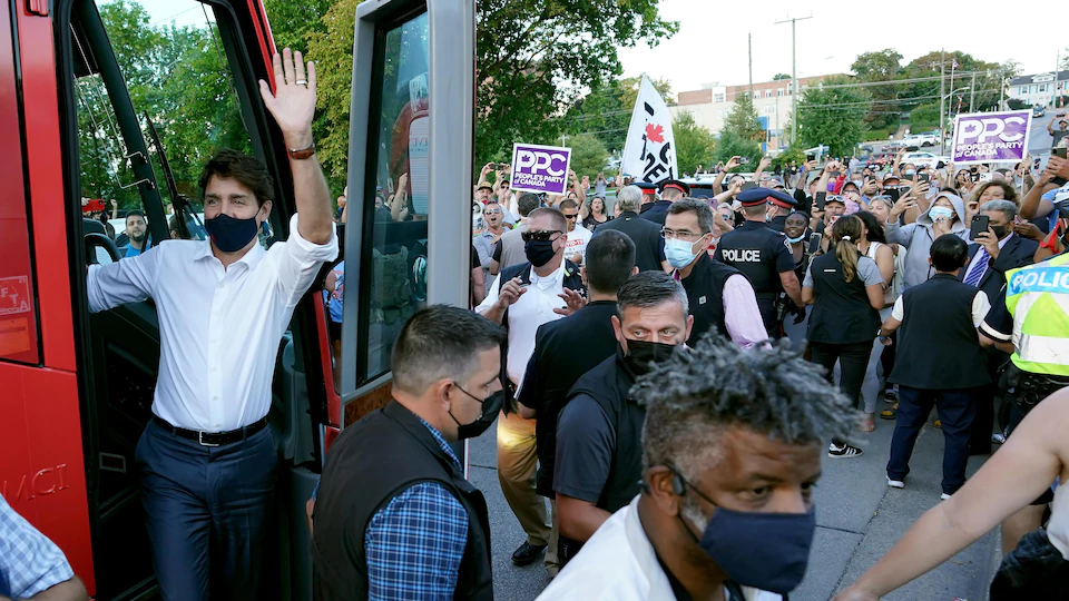 Justin Trudeau sort de l'autocar et salue la foule, protégé par des agents de sécurité. 