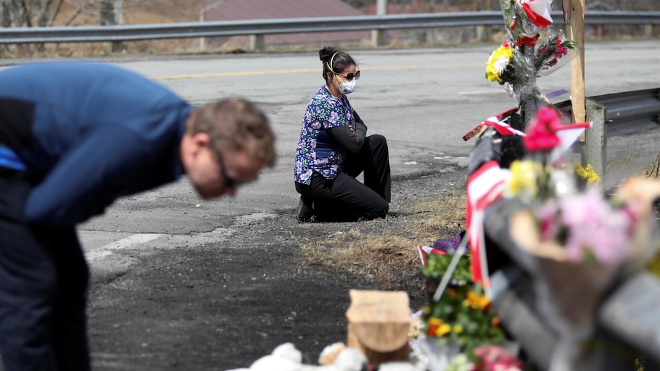 Une femme agenouillée devant un mémorial composé de fleurs autour d'un garde-fou en bordure de l'autoroute.