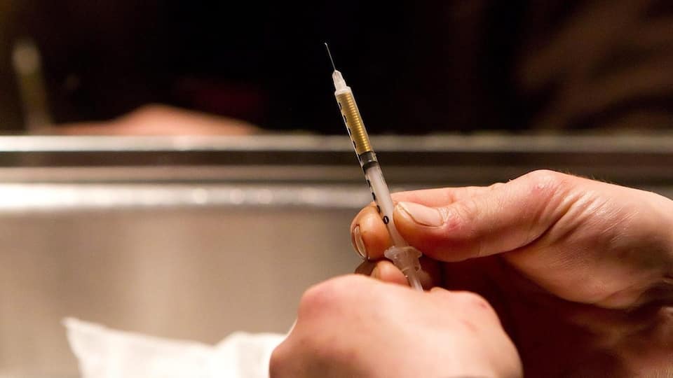 Un toxicomane se prépare à s'injecter de l'héroïne avec une seringue.