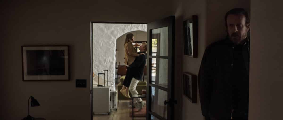 Lilly Collins et Jesse Plemons s'embrassent dans un couloir tandis que Jason Segal se cache au premier plan dans le film Netflix Windfall. 