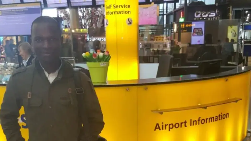 Tevin Obiga devant le comptoir d'un aéroport. 