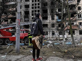 A teenager holds his guitar as he stands in front of a destroyed apartment building after it was shelled in the northwestern Obolon district of Kyiv.