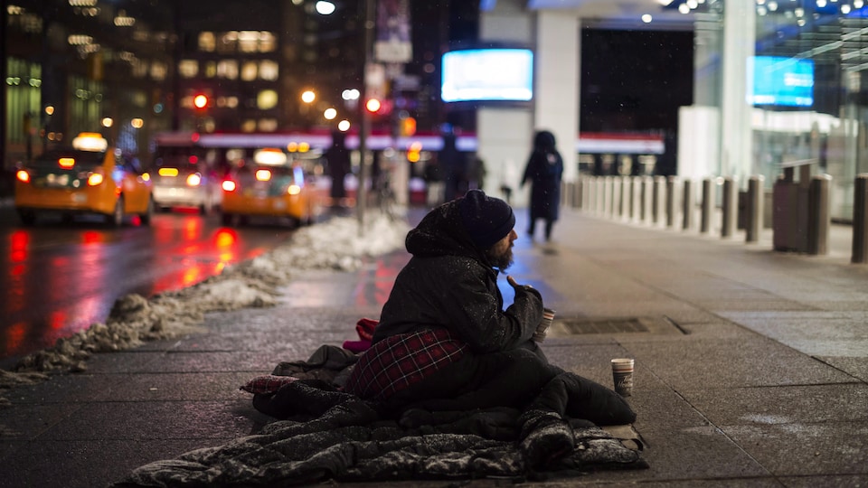 Une personne quête dans la rue, devant un édifice du centre-ville de Toronto.