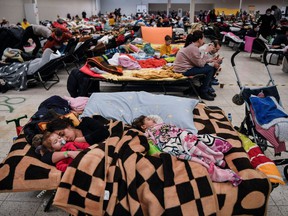 A mother sleeps with her children among many others in a temporary shelter hosting Ukrainian refugees located in a former shopping center near the Polish city of Przemysl, located close to the border with Ukraine, on March 8, 2022.