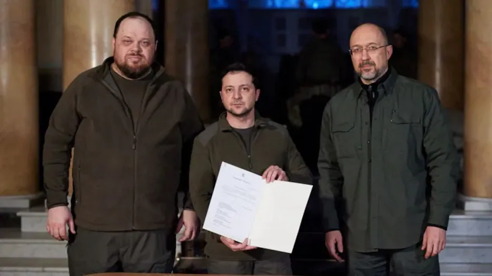 Trois hommes posent pour la caméra en tenant un décret.