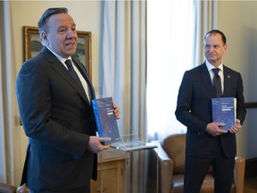 Quebec Premier François Legault , left, receives a copy of the provincial budget speech from Quebec Finance Minister Eric Girard Tuesday, March 22, 2022 at the Premier's office in Quebec City.
