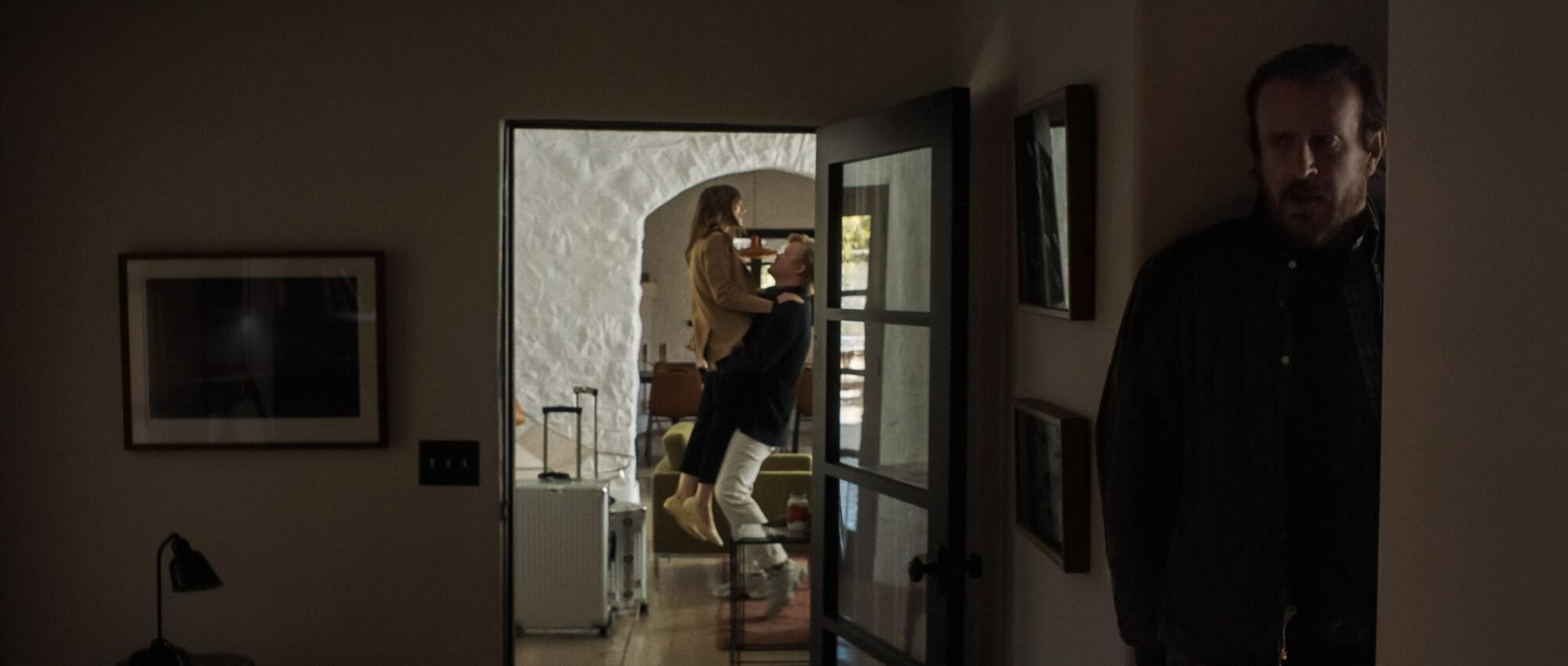 Un homme (Jason Segel comme "Personne") caché derrière un mur d'une femme (Lily Collins comme "Épouse") et un autre homme (Jesse Plemons comme "PDG") dans un plan fixe de "Aubaine."