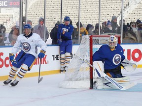 Sabers netminder Craig Anderson hugs the post as winger Vinnie Hinostroza (left) goes after the puck and defenseman Rasmus Dahlin looks on during yesterday's outdoor practice at Tim Hortons Field in Hamilton.