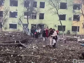 In this video grab from handout footage taken and released by the the National Police of Ukraine on March 9, 2022, people are helped out of a damaged building of a children's hospital following a Russian air strike in the southeastern city of Mariupol.