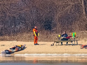 A US Coast Guard helicopter crew member waits while a woman kayaker speaks on her phone on Peche Island on Wednesday, March 17, 2020.