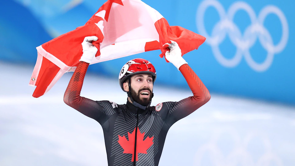 Steven Dubois sur la glace portant un drapeau du Canada au-dessus de sa tête.