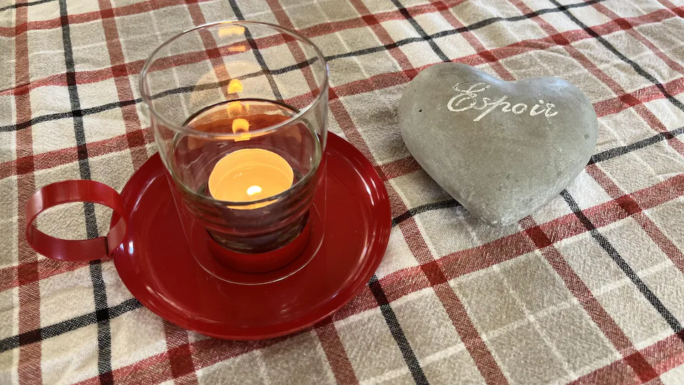 Une bougie et un caillou en forme de coeur avec le mot espoir, posés sur une nappe à carreaux.