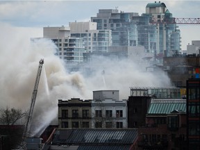 A firefighter on a ladder truck directs water on a four-alarm fire burning at a single room occupancy hotel, in Vancouver, BC, Monday, April 11, 2022.