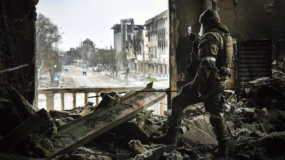 Un soldat russe s'arrête pour prendre une photo de la rue. Il se trouve dans les décombres d'une pièce d'un grand édifice.
