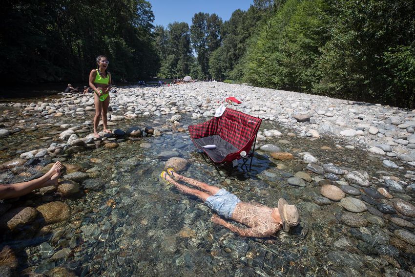 Albert Huynh cools off in the frigid Lynn Creek water as Leanne Opuyes, left, laughs in North Vancouver, BC, on Monday, June 28, 2021, during a deadly heat wave in British Columbia.