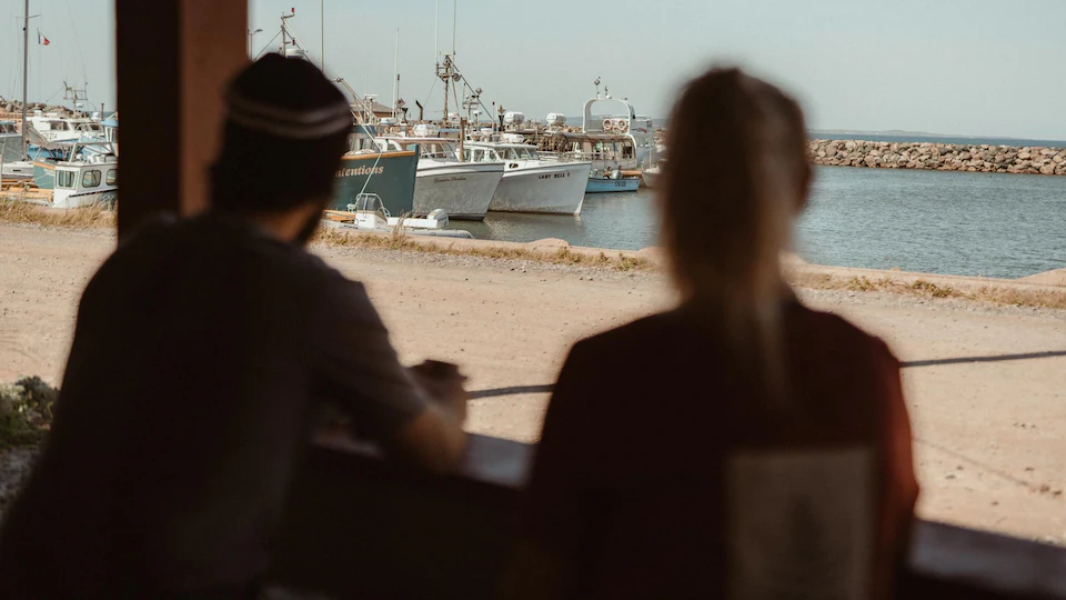 Un homme et une femme de dos, en train de prendre un café sur le quai de l'île d'Entrée.