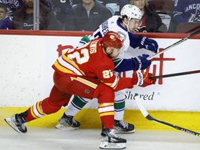 Vancouver Canucks defenseman Quinn Hughes, right, is checked by Calgary Flames center Trevor Lewis during first period NHL hockey action in Calgary, Saturday, April 23, 2022.