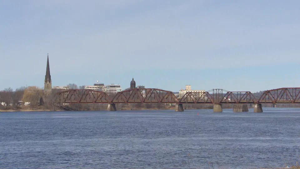 Un plan large de la ville de Fredericton, avec le fleuve Saint-Jean. Un pont enjambe la rivière. 
