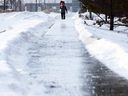 A pedestrian walks along an ice covered sidewalk as he carries traffic cones to a two vehicle collision, in Edmonton on Monday, Jan. 17, 2022. 