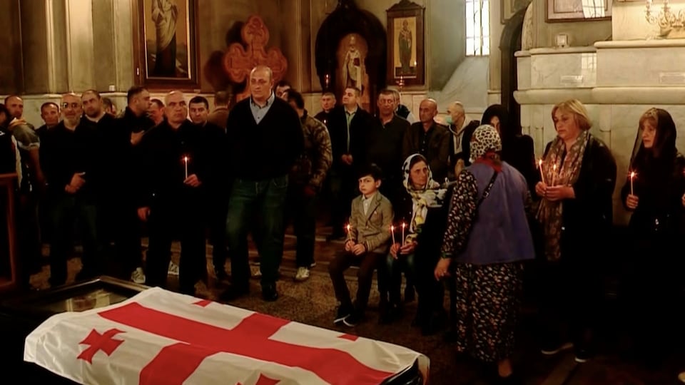 A crowd gathered around a coffin draped in the Georgian flag in a church.