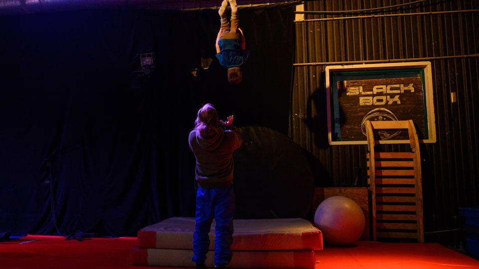 A child performs a somersault in the air while a man reaches out his hands to catch him.