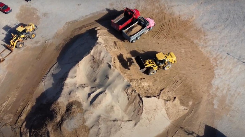 Aerial view of a massive pile of sand with a loader and trucks being filled.