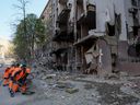 Communal workers clean an area around a building destroyed in an air strike, amid Russia's invasion of Ukraine, in Kyiv, Friday, April 29, 2022.