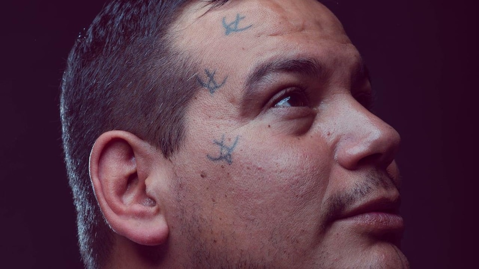 A man poses for the photo with three small bird tattoos on his face.
