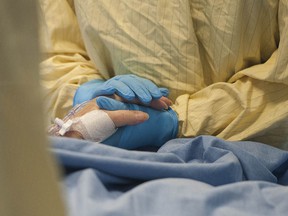 An intensive-care nurse holds a COVID-19 patient's hand at Surrey Memorial Hospital in a file photo from June 2021.