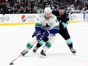 Tucker Poolman, left, shielding the puck against the Seattle Kraken's Ryan Donato, has been limited to 40 of the Canucks' 70 games this season.