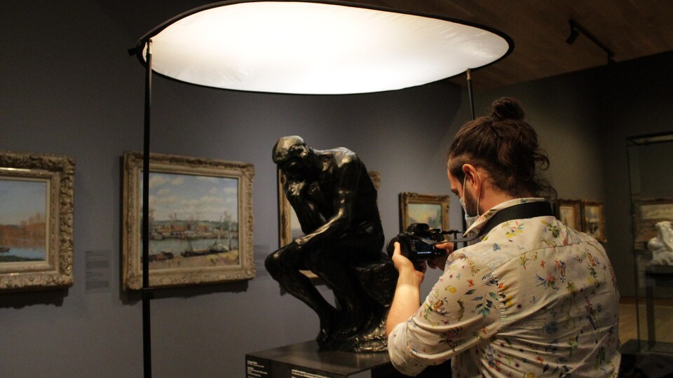 Un homme prend des photos détaillées d'une sculpture du «Penseur» de Rodin dans une salle d'un musée. 