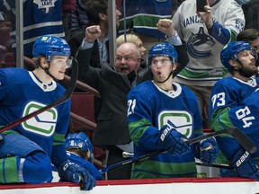 Head coach Bruce Boudreau, arms raised in celebration behind the Canucks bench after a Rogers Arena win earlier this season, 'makes the team feel good' with his positive energy.