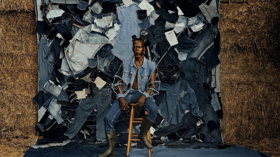Artists dressed head to toe in jeans sit in front of a collage of scraps of jeans and haystacks. 