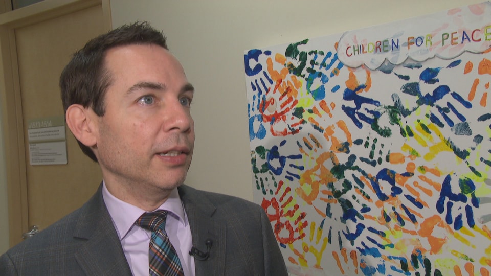 Alex Munter interviewed in a corridor in front of a work of art painted by children's hands.