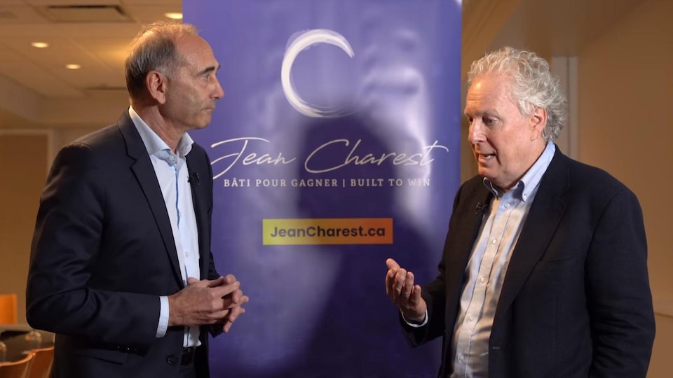 The two men chat in front of Jean Charest's campaign poster.