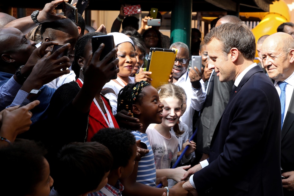 Emmanuel Macron takes a walkabout in Nigeria.  A little girl takes his hands and looks up at him in admiration.